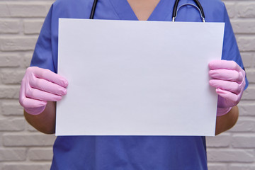 A female doctor holds an empty blank sheet, copy space for the text. Hands of a nurse in protective...