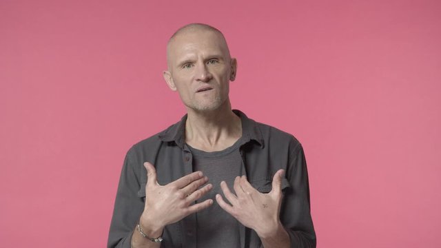 Middle-aged angry bald guy with bristle offended with disrespect, pointing himself, saying cursing words, sick and tired or ignorant people, having argument, starting fight at bar, pink background