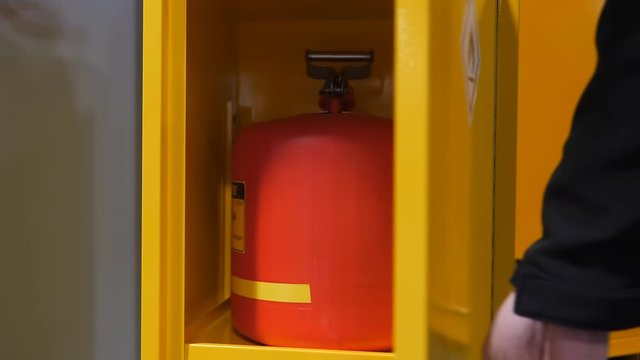 Man's hand opening yellow color metal box container with gas cylinder in it, safe storage for keeping flammable substances and materials marked with flame symbol sticker.