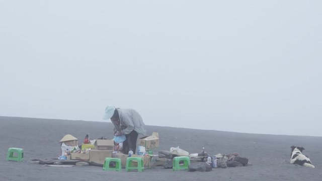 EAST JAVA - Indonesia. April 16, 2020: Poverty concept. Poor old woman selling drinks and snacks on the sea of sand at Mount Bromo national park. Shot in 4k resolution