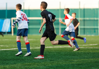 Obraz na płótnie Canvas Boys in white black sportswear running on soccer field. Young footballers dribble and kick football ball in game. Training, active lifestyle, sport, children activity concept