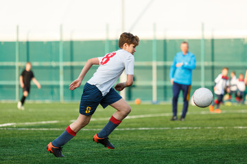 Boys in white black sportswear running on soccer field. Young footballers dribble and kick football ball in game. Training, active lifestyle, sport, children activity concept