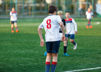 Boys in white black sportswear running on soccer field. Young footballers dribble and kick football ball in game. Training, active lifestyle, sport, children activity concept
