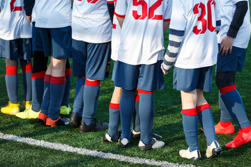 Boys in white sportswear running on soccer field. Young footballers dribble and kick football ball...