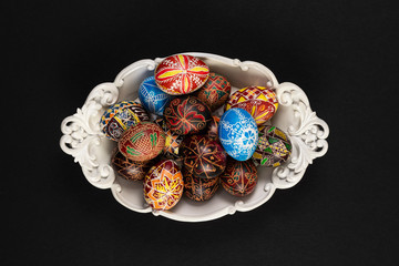 Easter eggs painted in traditional Eastern European style with a floral/geometric design in a bowl isolated on a black background.