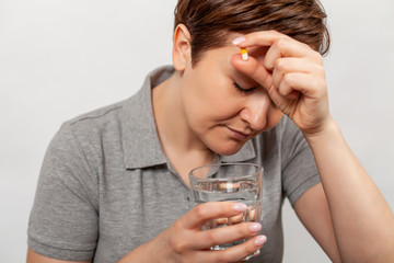 A woman is not feeling well, holding a glass of water and pills, doubting the need to take medicine...