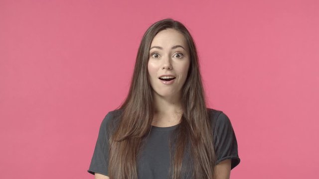 Surprised attractive caucasian brunette, looking camera casual normal face then see something intriguing, open eyes and smiling amused, excited hear great good news, cheerfully react, pink background