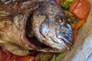 Closeup of the head of a baked dorado fish with lemon and vegetables.