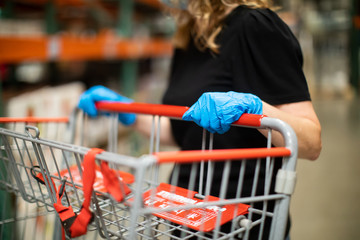A woman shopping for groceries and necessities for her family inside a warehouse-style store during the pandemic Covid-19 coronavirus pandemic and she is wearing a face mask and latex rubber gloves