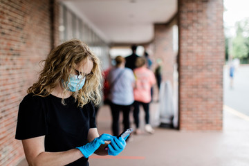 A woman who is waiting in a long line outside of a grocery store during the pandemic Covid-19 coronavirus pandemic. She is wearing a face mask and latex rubber gloves for protection from airborne and 