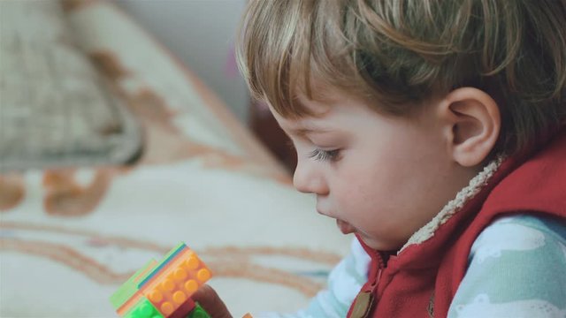 Little charming boy with blue eyes playing with the constructor toys on couch in living room. Close up, 4K