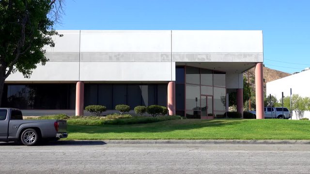 The front and side of a generic and unmarked office building exterior are shown during a sunny day.
