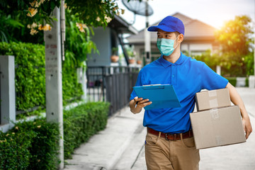 Asian delivery man in blue t-shirt carrying parcel box and document to sign in front of customer home. Delivery man concept.