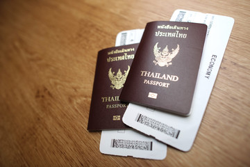 A foreign passport of Thailand with a plane ticket is placed on a wooden table.