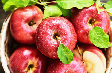A lot of fresh Royal Red Gala apples with green leaf and water drop in basket on wooden background.
