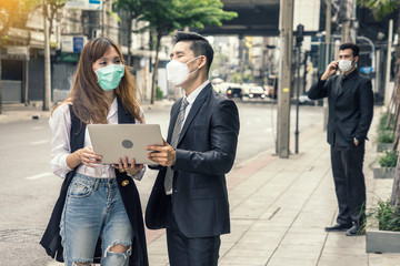 Asian women walk to talk with colleagues, find work, and there are men standing on the mobile phone behind and walking, creating social distance.
