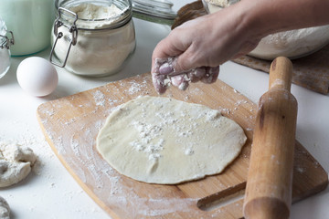 A woman rolls the dough into a tortilla on a wooden board, next to flour, eggs, milk. Russian cuisine