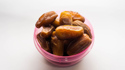 Dates or kurma in purple plastic container on isolated white background.