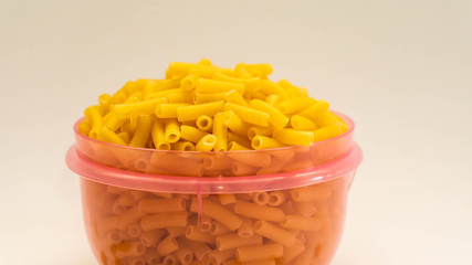 Closes up of full purple plastic container of raw macaroni on isolated white background.