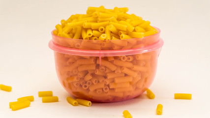 Closes up of full purple plastic container of raw macaroni on isolated white background.