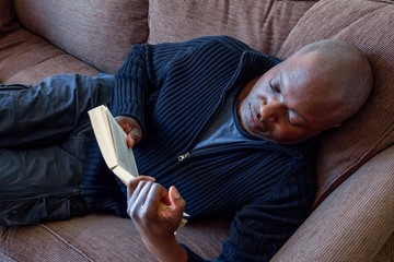 Black man, of African ethnicity, reading on the sofa