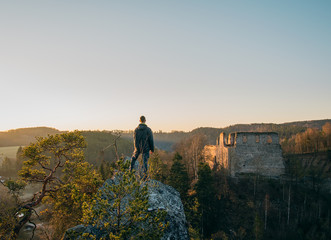 Young man in jacket, pants standing and looking to ruin Divci kamen from rock. Czech republic © Space Creator