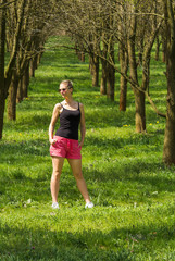 Attractive young blonde caucasian woman in sunglasses standing on spring tree avenue with grass