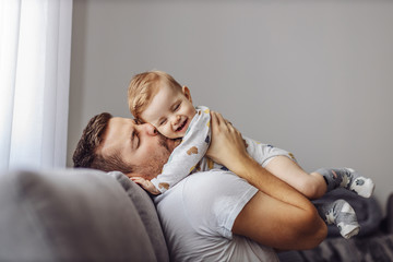 Adorable little blond boy playing with his caring father and biting his nose. Father is smiling. - obrazy, fototapety, plakaty