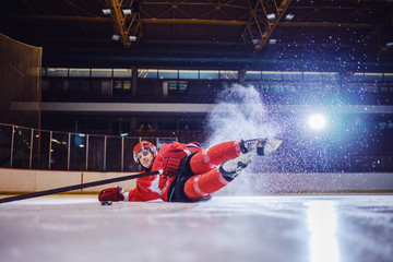 Strong hockey player falling on ice in attempt to receive puck from teammate.