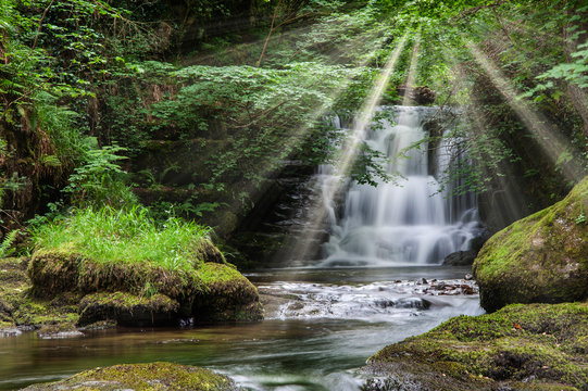 Majestic waterfall in forest landscape image with added drama of sun beams breaking through trees in woodland