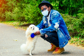 afro man in mask hugging his fluffy spitz in park