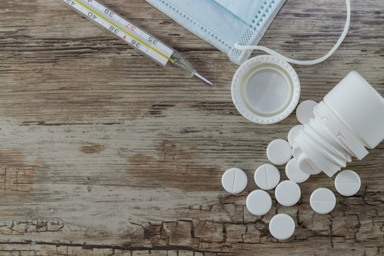 Tablets in a white jar, a thermometer, a medical mask to protect against flu and  viral diseases. Protective mask on a wooden background against the spread of coronavirus and epidemic. Coronavirus