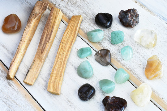A close up image of palo santo smudge sticks and healing crystals on a white wooden table. 