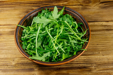 Fresh green arugula in ceramic bowl on a wooden table. Healthy food or vegetarian concept