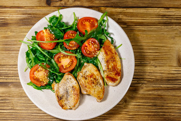 Fried chicken breast with salad of fresh arugula and cherry tomatoes on wooden table. Top view