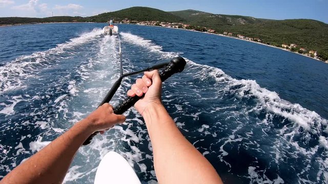 First person view of a man being towed by a speed boat on a wake board 