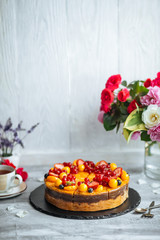 Side view on organic tangerine cake decorated with berries on the light grey background with a cup of tea, vertical