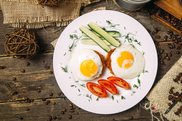 Top view on cutlets with fried eggs, cucumber and tomato on a plate on the wooden table, horizontal