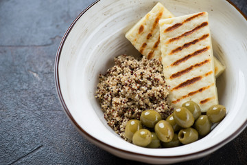 Close-up of quinoa with roasted cheese and green olives served in a white bowl, selective focus