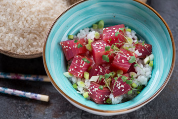 Poke bowl with tuna and raw white rice in the background, studio shot on a grey stone background