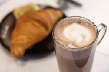 closeup hot cocoa or chocolate and mocha with milk froth in clear glass cup and croissant bread on table in cafe restaurant and coffee shop for breakfast or snack and morning drink background on warm