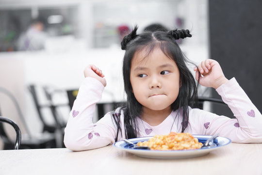 Asian child cute or kid girl anorexia or sad and bored food or untasty boredom with frown on wood table for breakfast or lunch eating at restaurant or food court and canteen on preschool or nursery