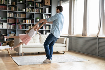 Father spinning little daughter have fun spend time at home. Small girl wears dress, crown on head...
