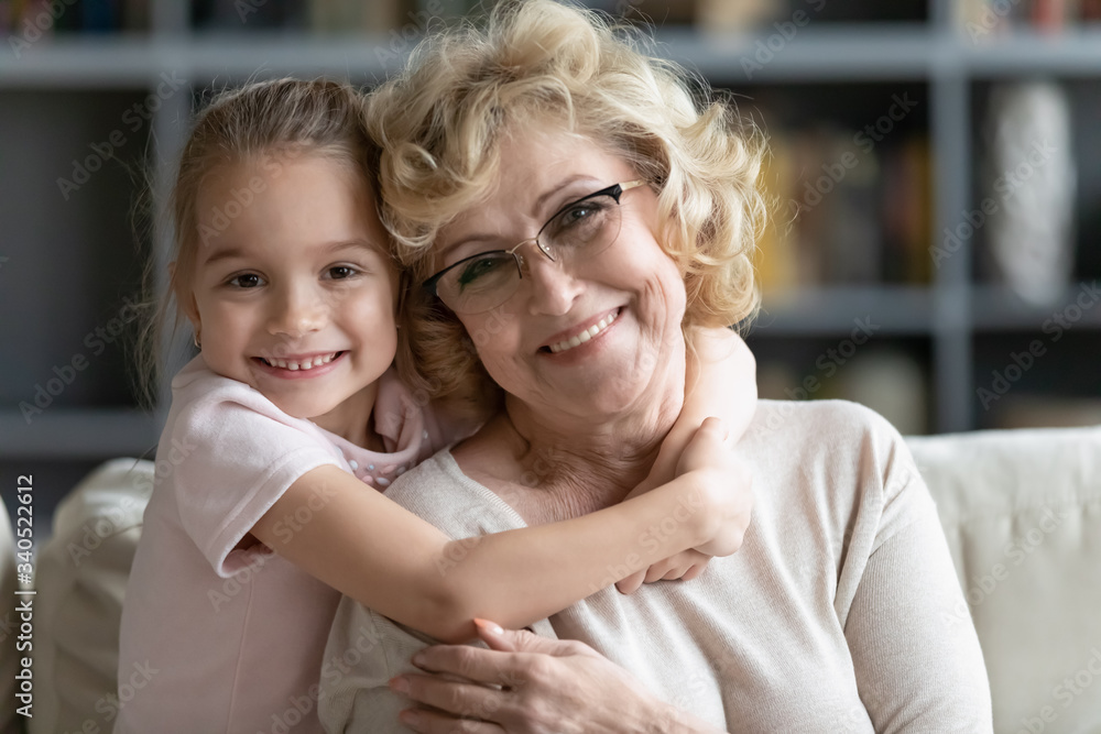 Wall mural multi-generational family portrait. little granddaughter hugs grandma sit on sofa in living room smi