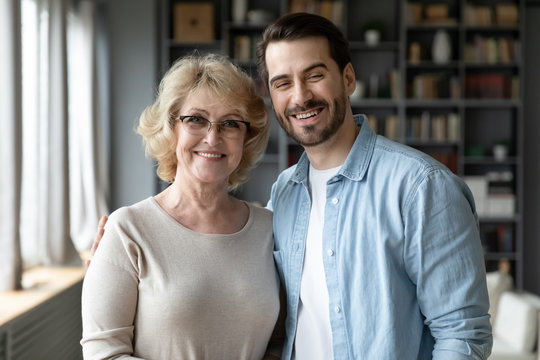 Happy senior mother in eyeglasses and bearded grown up son standing posing looking at camera. Different ages, multi-generational family portrait, next generation and offspring, familial values concept