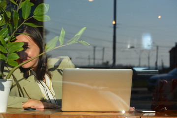 A beautiful young woman is sitting in a cafe with a laptop and a sly smile.