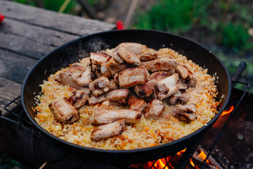 Rice with pork ribs in a cast iron skillet over a fire. Pilaf is cooked in a cast-iron pan. Pilaf is a traditional Middle Eastern and Asian food.