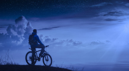 Naklejka na ściany i meble Cyclist on a mountain top at night