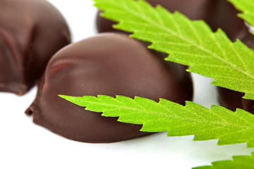 Sweet cannabis candy containing CBD cannabidiol, green marijuana leaves on white isolated background. Candy with the addition of medical cannabis CBD for recreational use to relax the body and mind