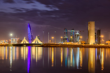 Fototapeta na wymiar Beautiful view of iconic building Bahrain World Trade Center and Shaikh Isa Bin Salman Causeway Bridge at blue hour after sunset with striking clouds, Manama, Bahrain